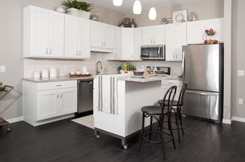 Contemporary kitchen with white cabinetry, pendant lighting, and stainless steel appliances. Kitchen island is the focal point of the kitchen area with seating for entertaining.